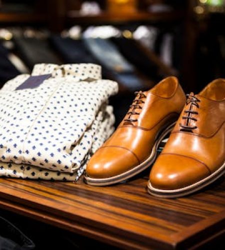 Elegant brown leather shoes and printed shirt displayed on a wooden table in a stylish clothing store.